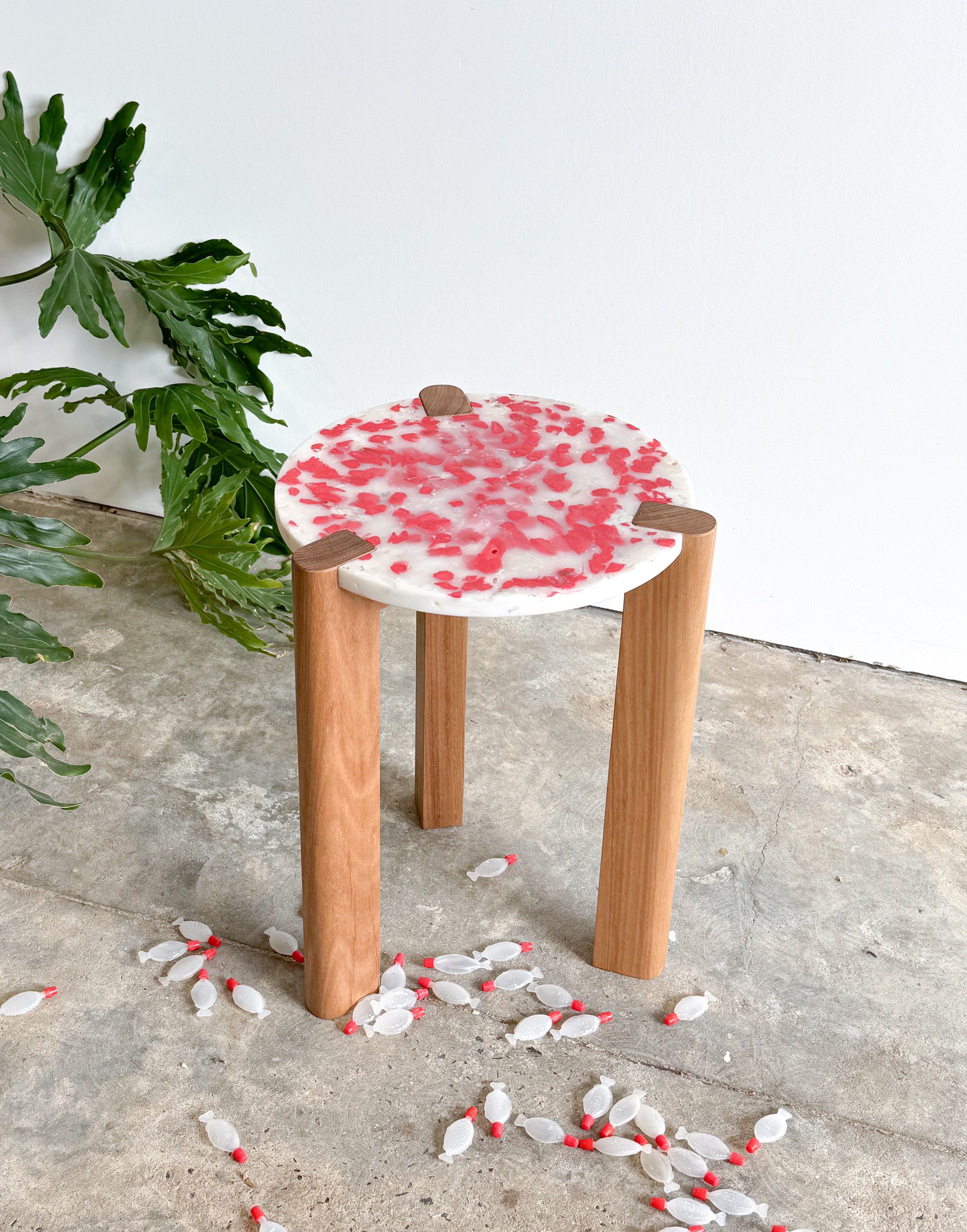 Short stool with 3 Tasmanian Oak timber legs and a red and white seat made from recycled soy sauce fish and milk bottles